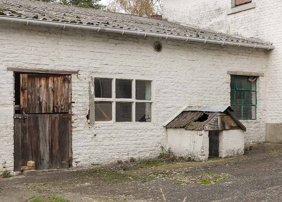 An abandoned farmhouse with a dilapidated dog kennel