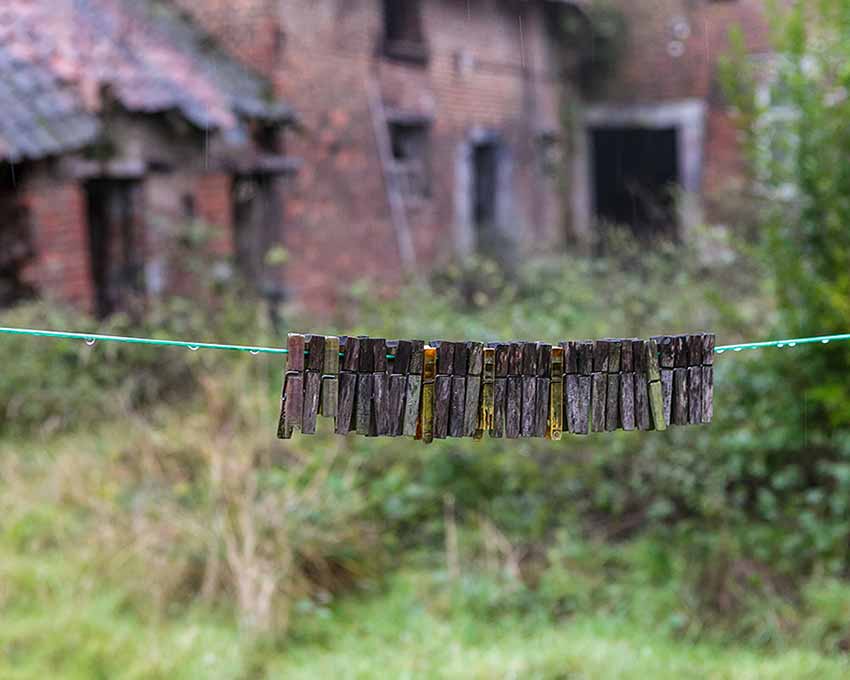 A row of clothespins on a clothesline near an abandoned house