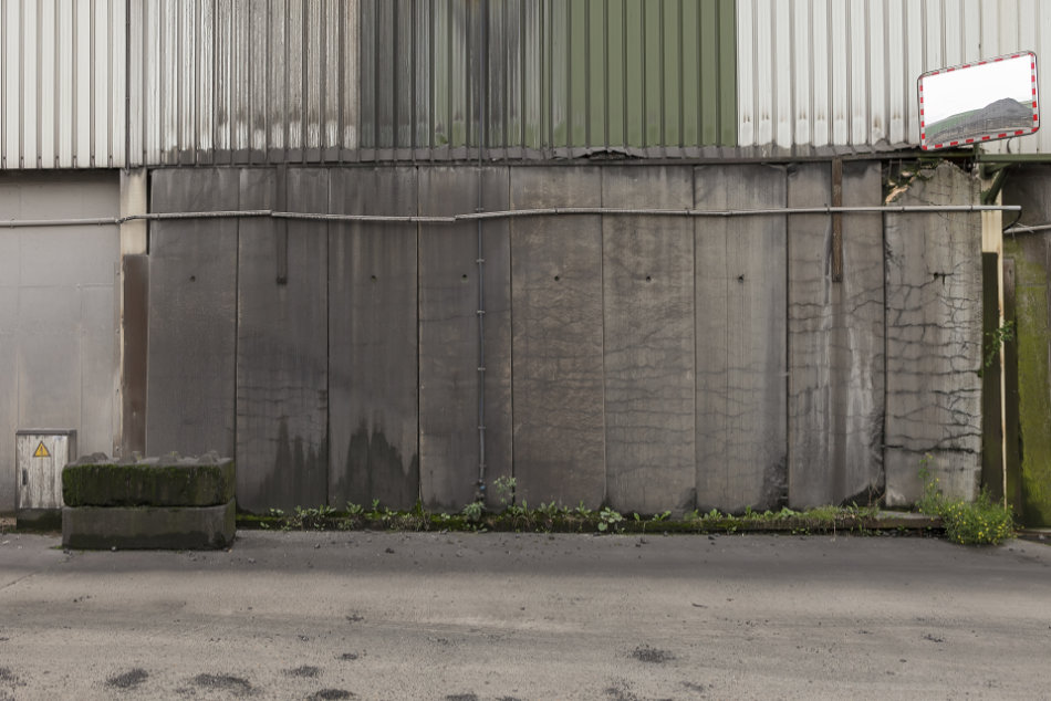 An abandoned industrial area with a traffic mirror showing a view of hills