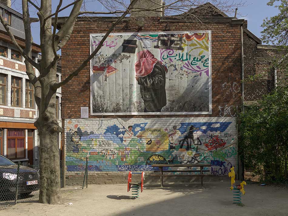 A children's playground in front of a billboard about refugees.