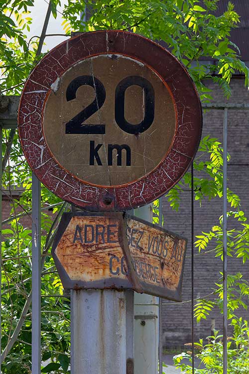A weathered 20 km/h speed limit sign: "Address the concierge"
