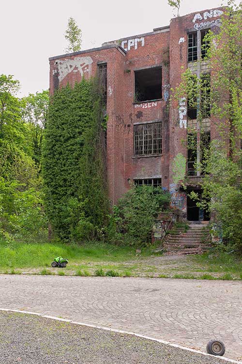 A toy tractor and a broken wheel in front of a dilapidated barracks